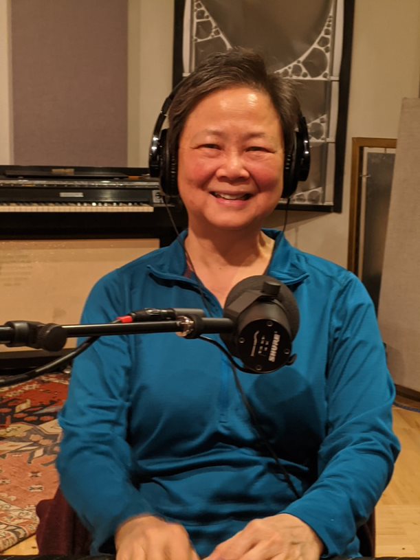 Wei-Zen Wei sitting in front of a microphone wearing headphones and blue long-sleeve blouse