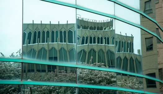 Reflection of the College of Education from the round glass of the Faculty Administration Building in spring with flowering trees