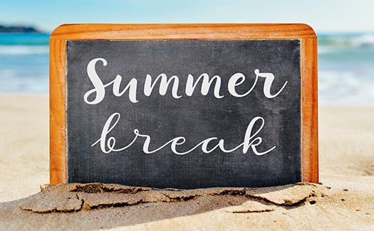 a chalkboard saying 'summer break' is half buried in the sand on a sunny beach