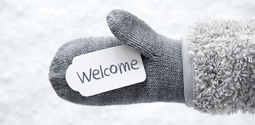 a mittened hand holds a tag that says welcome in front of a snowy background